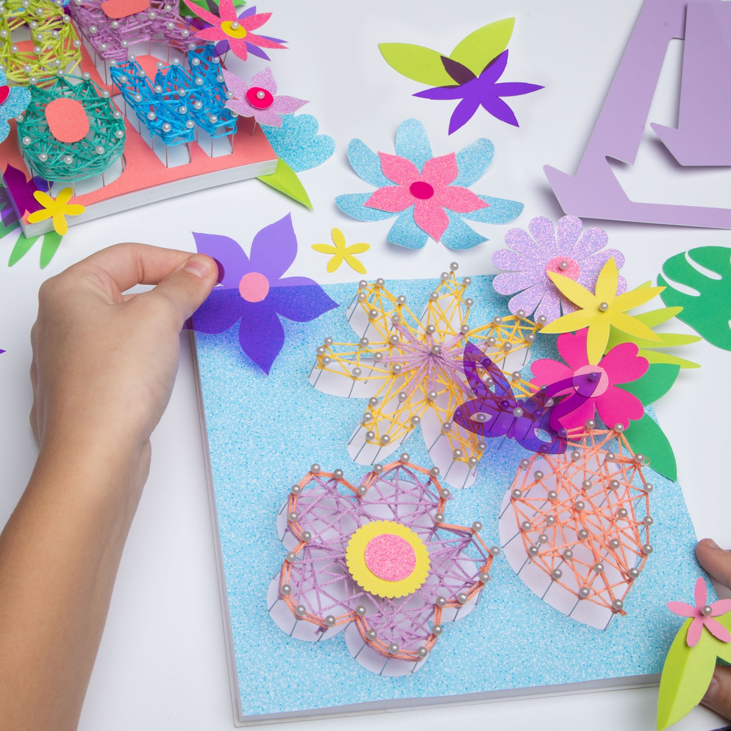 Child's hand holding a purple flower over the flower string art as they decide where to place.