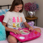 Young girl sitting on a bed using a pink craft board with colorful items.