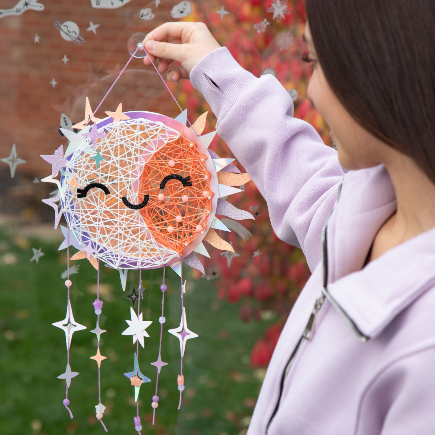 Celestial Sun/Moon String art being hung on a window by a child.